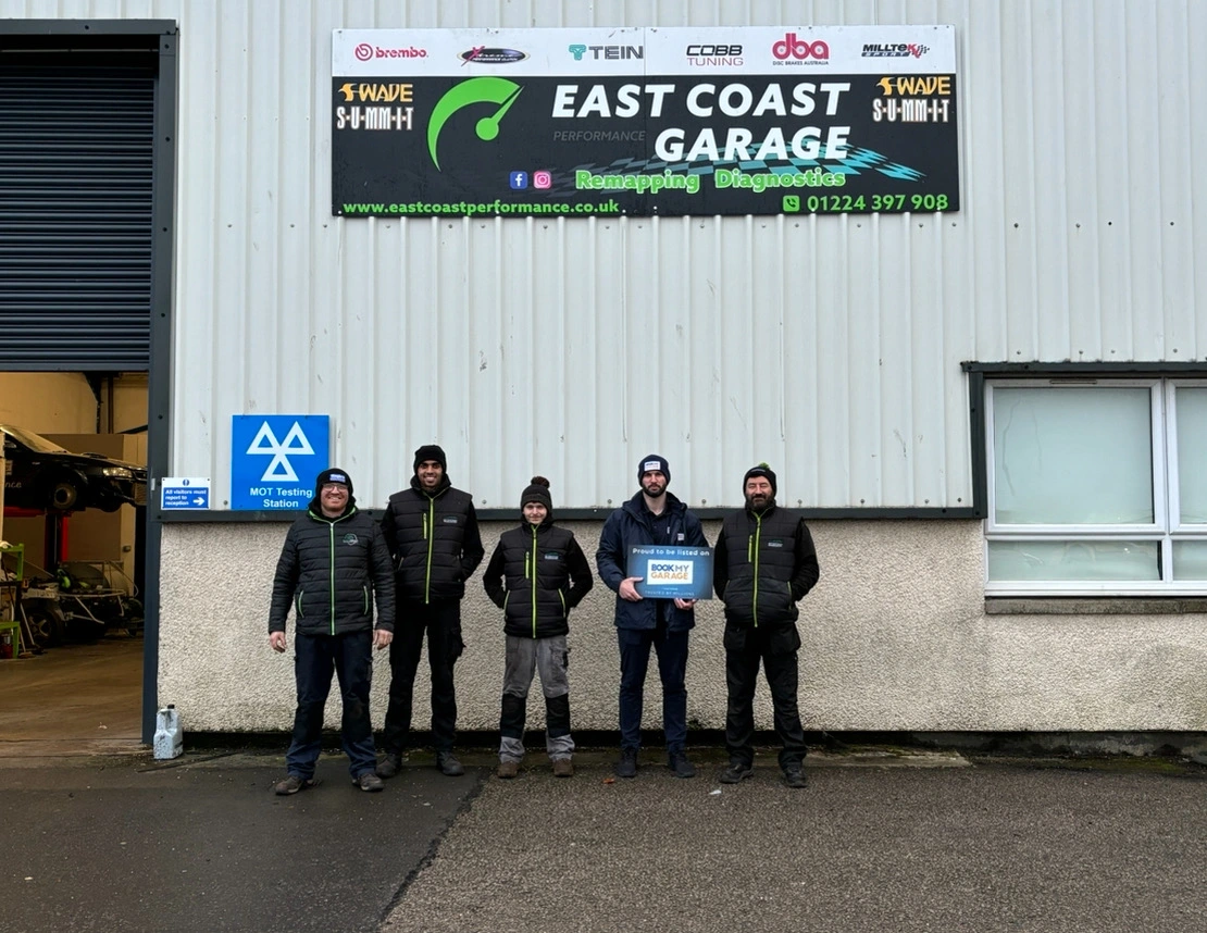BookMyGarage employee standing outside East Coast garage with four members of garage staff holding BookMyGarage branded card.
